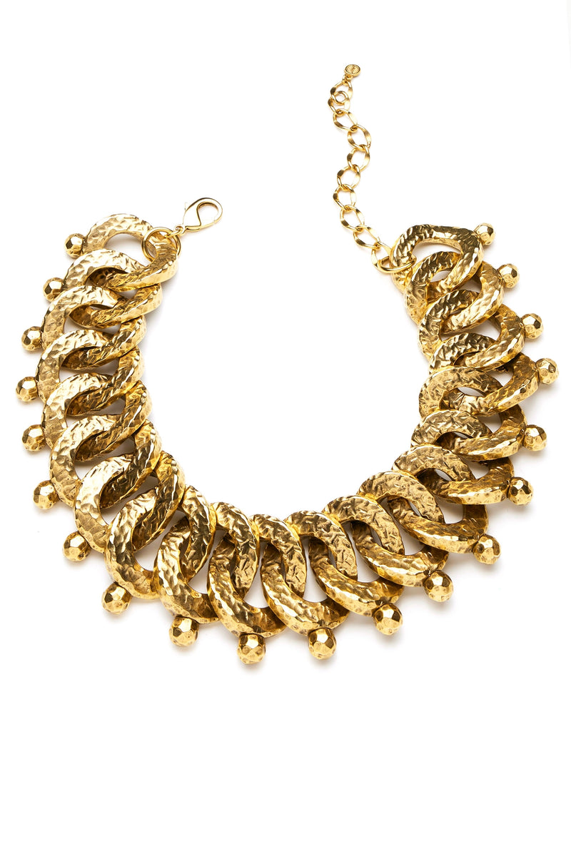 A hand-hammered gold necklace with individually made links, featuring a textured pattern and hanging gold elements.